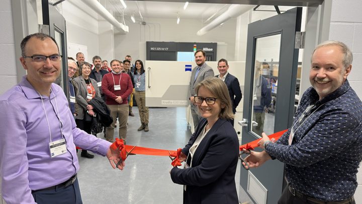 Two men and a woman standing in front of an open room cutting a red ribbon in the opening while smiling at the camera. An X-ray microscope can be seen in the background with other people smiling at the camera