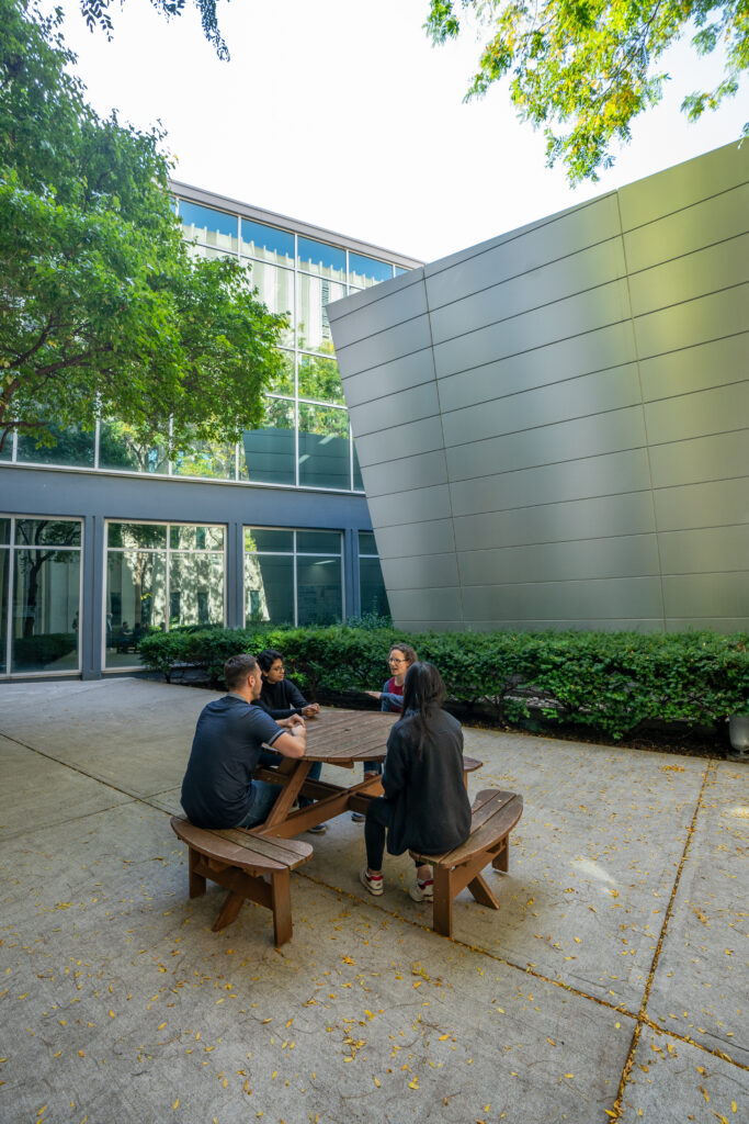 4 staff members sitting at picnic table in CCEM courtyard.